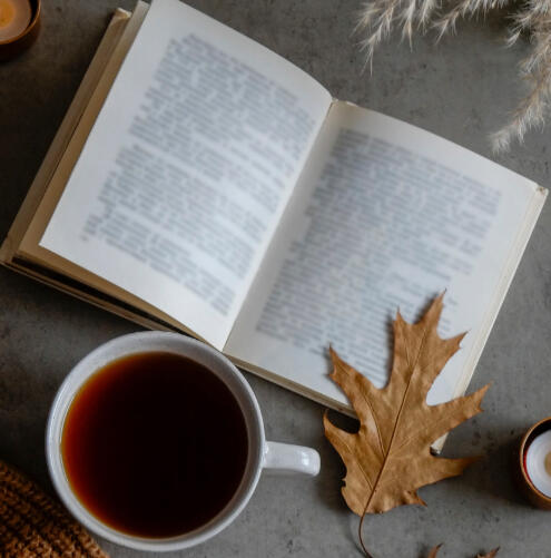 An open book with an orange oak leaf resting on the page and a cup of tea