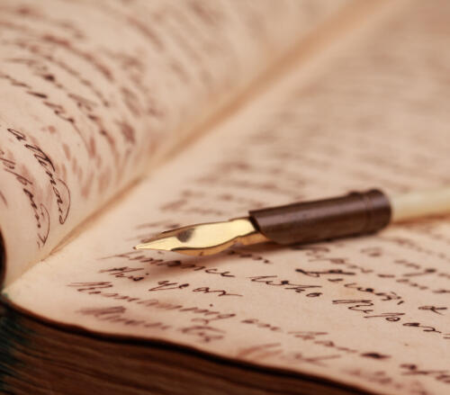 An open book with cursive handwritten pages and a vintage ink pen resting on the page